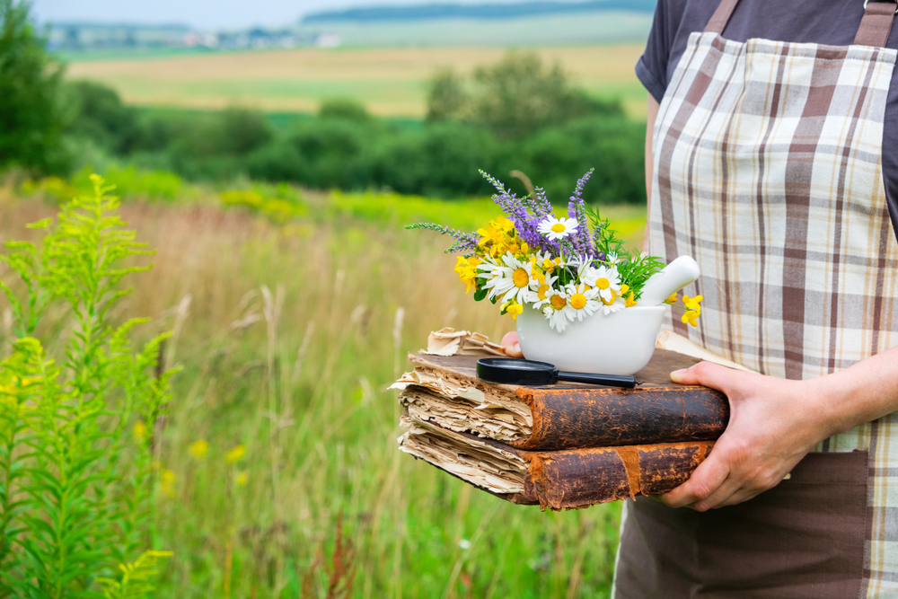 Woman in field with bowl of herbs and books